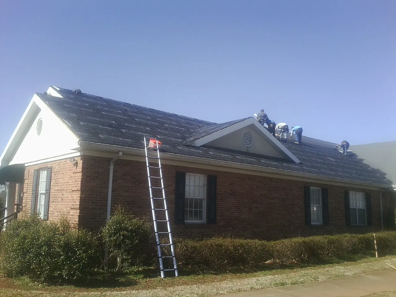 Crew tearing shingles off a brick ranch roof with a ladder set — Metal Roof Repair work by our crew in Fountain Valley