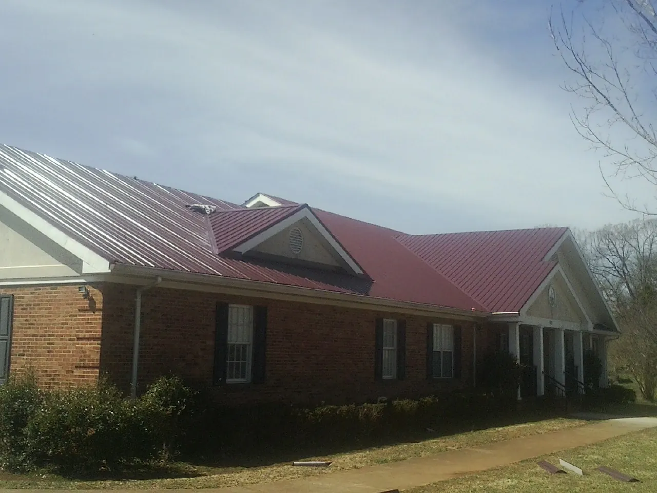 Red metal roof with gabled entries on a long brick building, from a Hail Damage Roof Repair job in Fountain Valley