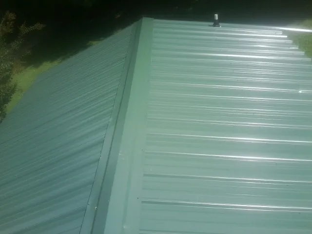 New green metal panels meeting at the ridge of a roof — Flat Roof Repair work by our crew in Fountain Valley