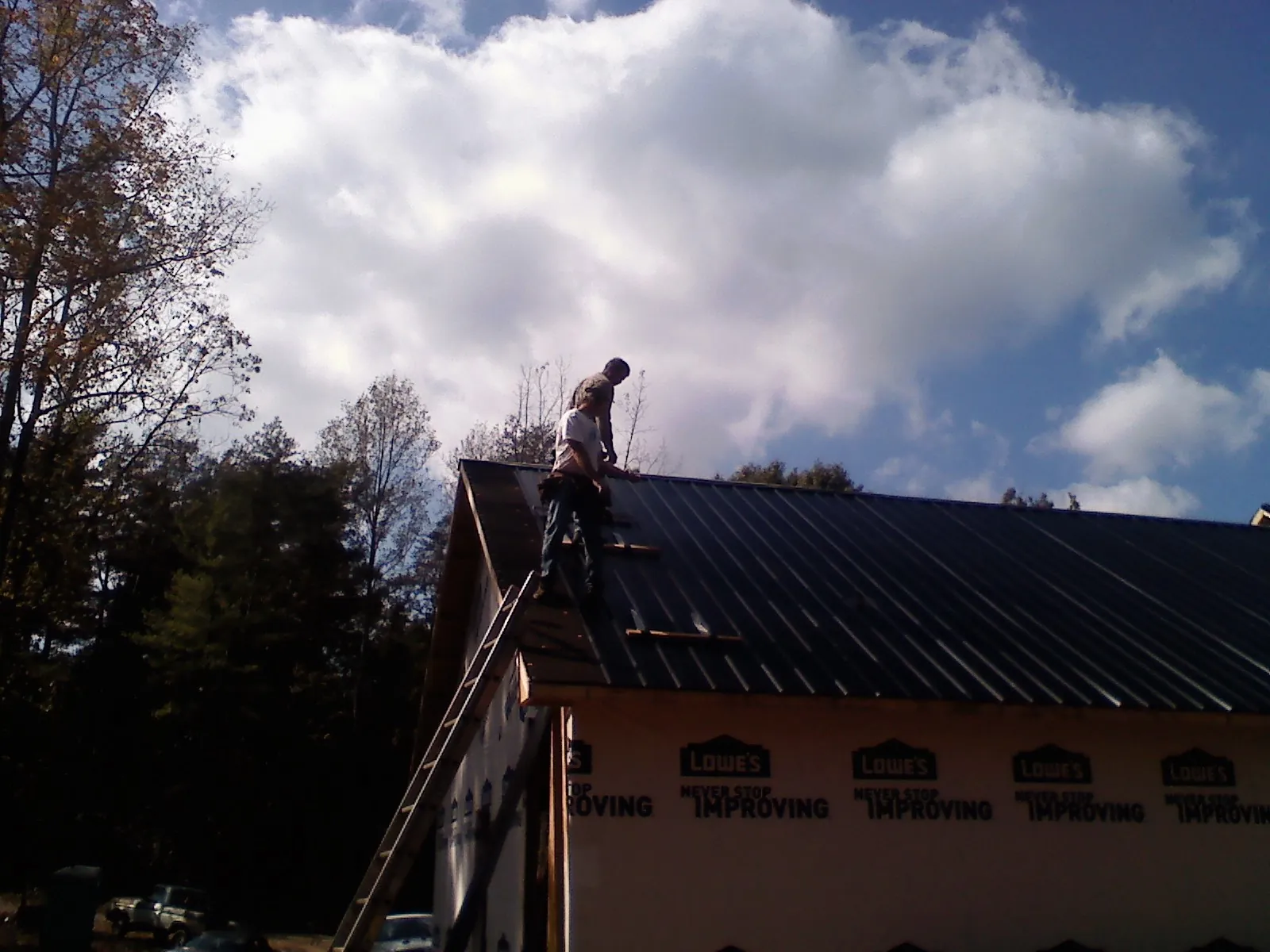 Roofer fastening dark metal panels high against a cloudy sky, from a Roof Inspection job in Fountain Valley