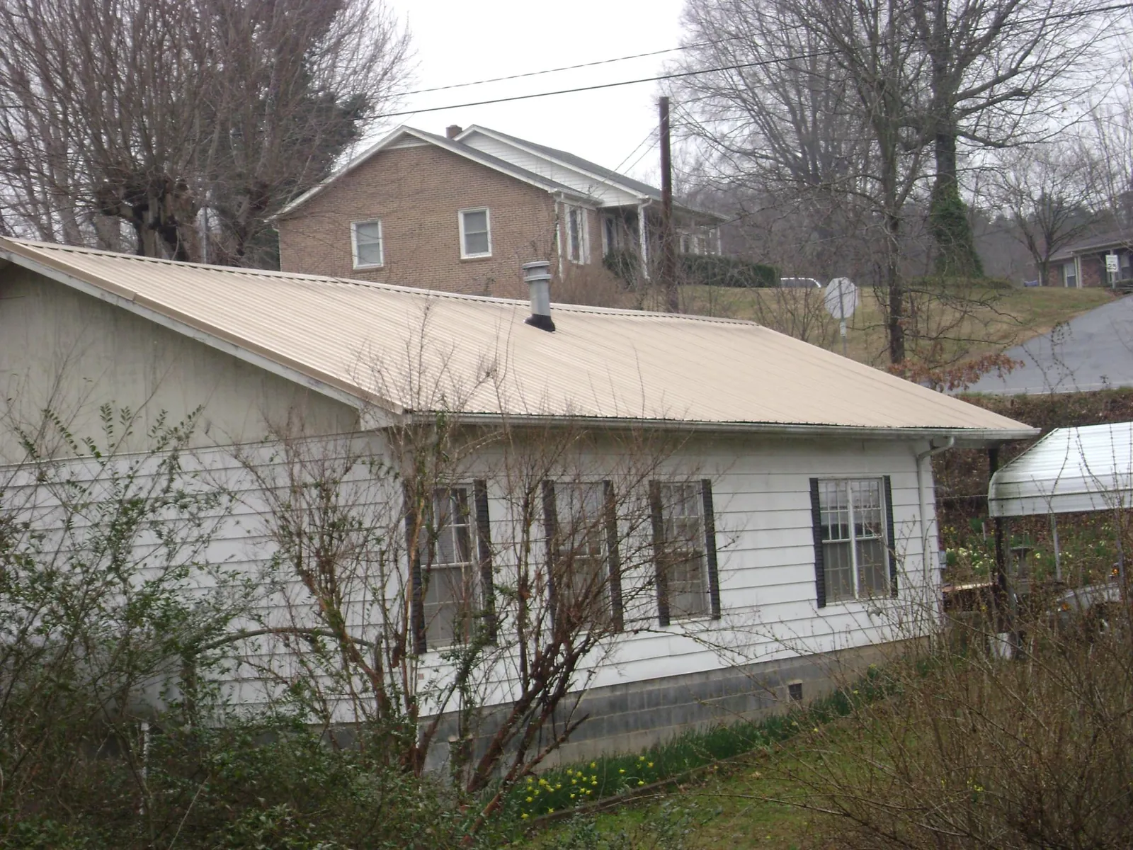 Tan metal roof on a white sided house set into a hillside — Commercial Roofing by Roofing Brothers in Fountain Valley